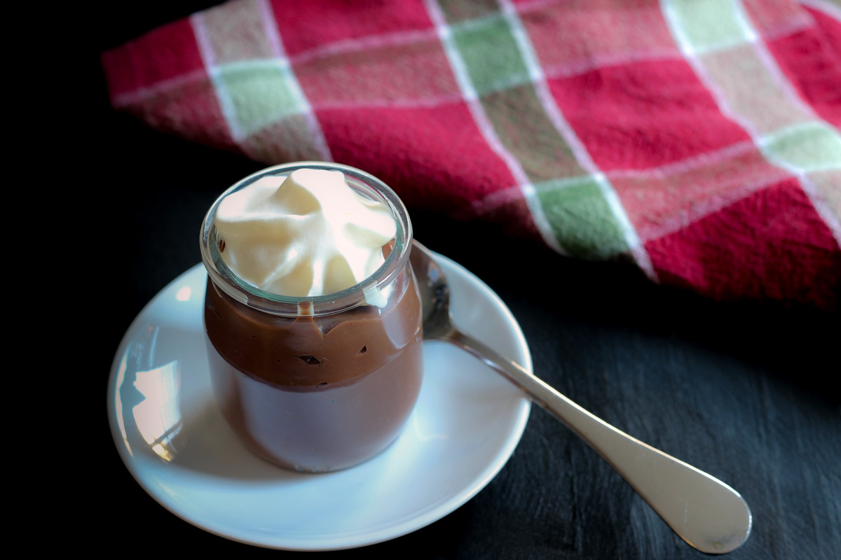 ramekin of chocolate pudding topped with whipped cream on a white dish with a spoon.