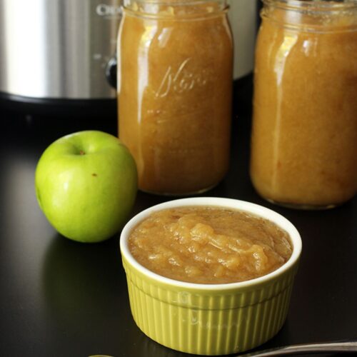 dish of applesauce with full jars and a green apple.