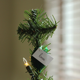 A cross at the top of a Christmas tree with a love ornament and lights.