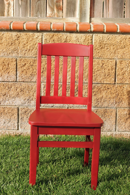 A wooden chair on the grass near a brick wall.