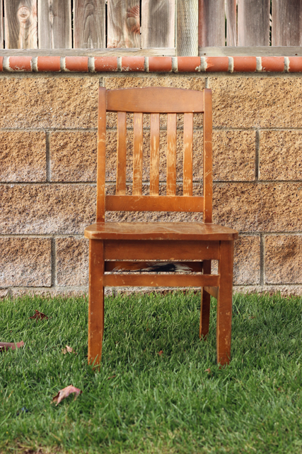 A chair sitting on the grass in front of a brick wall.