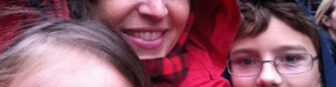 A mom wearing a red hood with kids,  smiling at the camera.