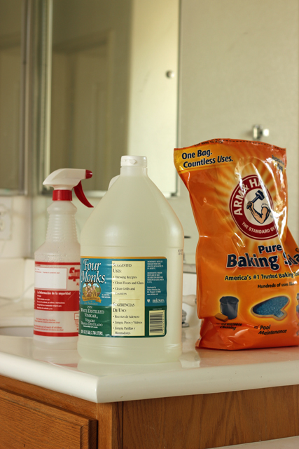 spray bottle, bottle of vinegar, and bag of baking soda on bathroom counter.