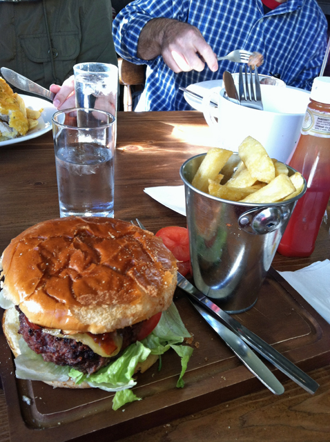 A burger sitting on top of a table with a bucket of chips.