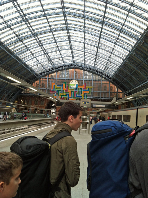 A group of kids boarding a train with heavy backpacks on.