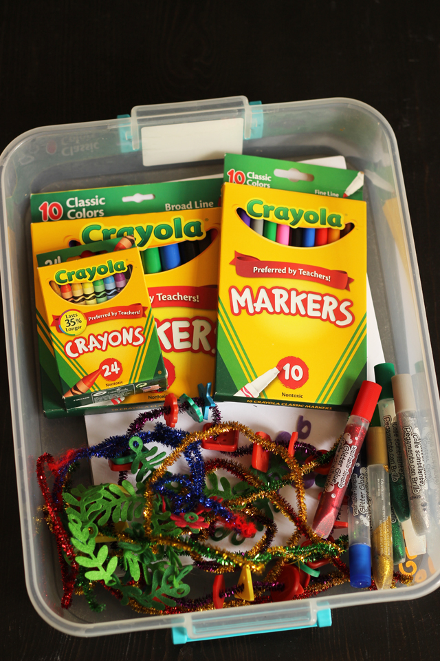 craft supplies box with glitter glue, markers, crayons, and pipe cleaners.