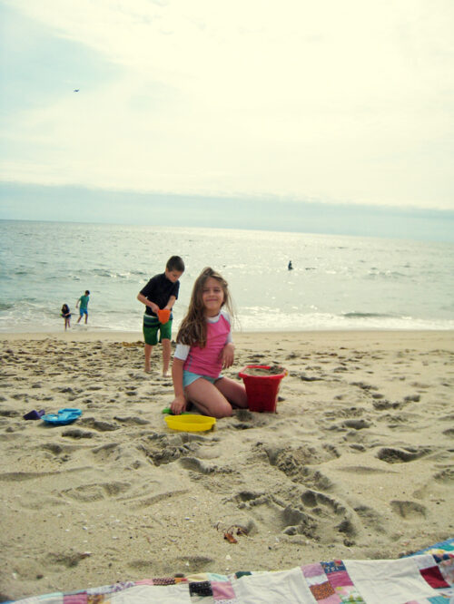 Kids sitting at a beach with sand pails.