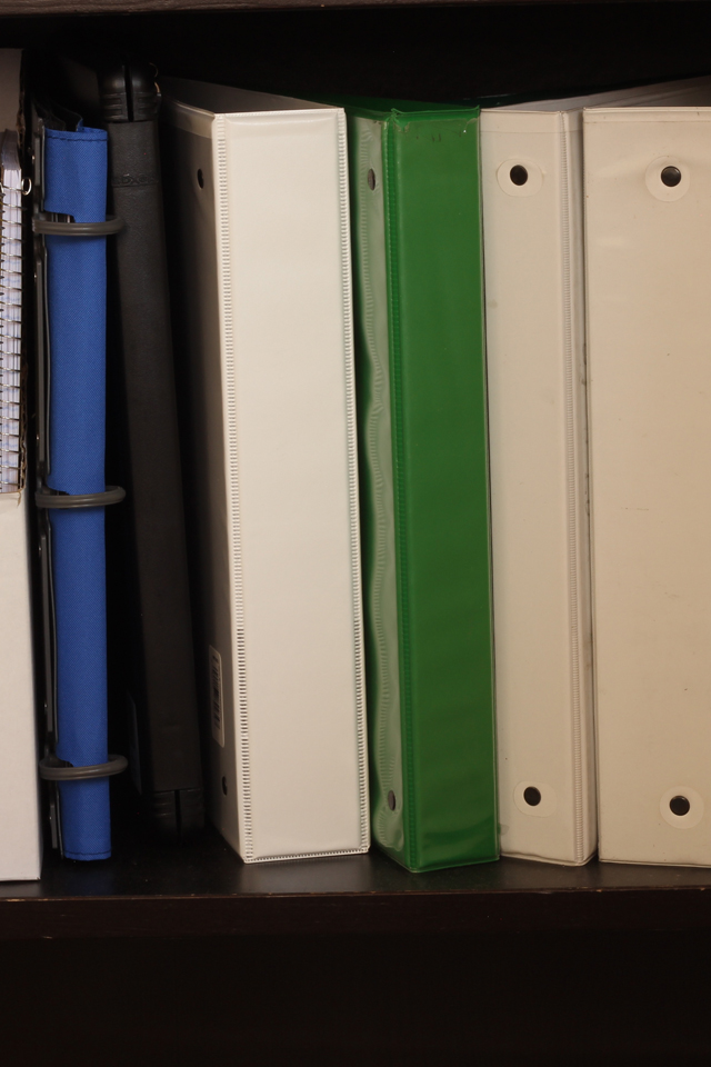 White, blue, green, and black binders lined up on a shelf.