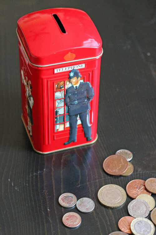 A close up of a bank in the shape of a British call box with coins.