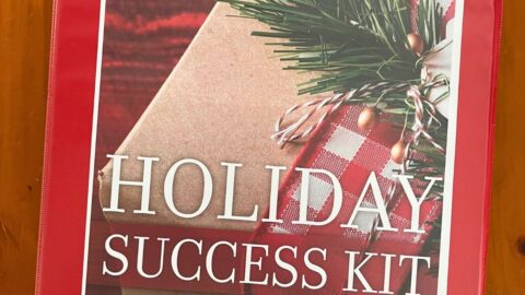 red binder housing holiday success kit on wooden surface.