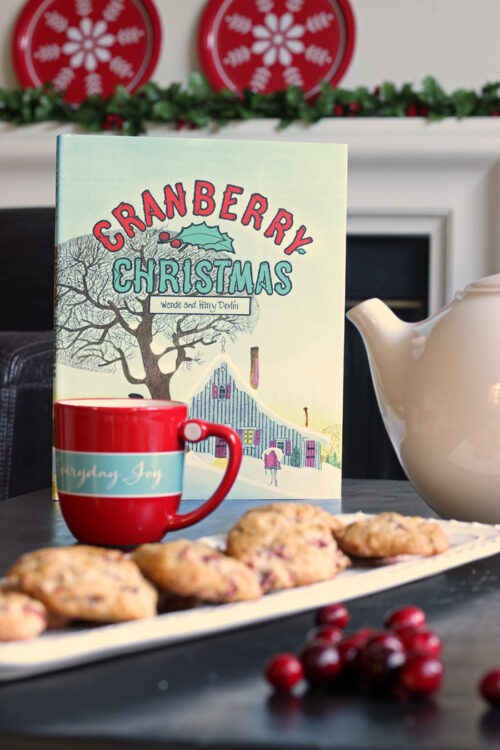 Cranberry Christmas book standing up on table next to mug, tea pot, and platter of cookies.