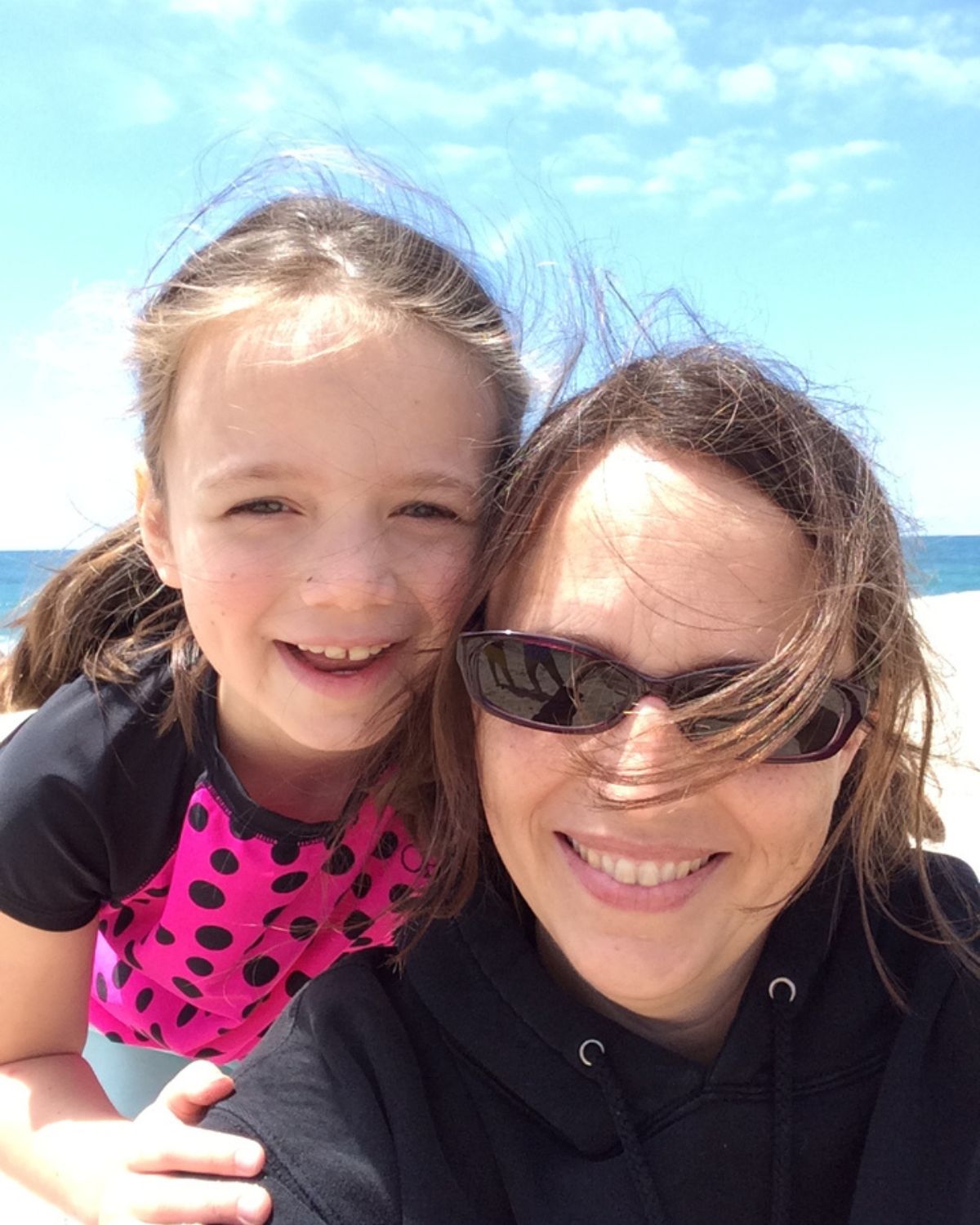 girl and mom at the beach smiling at camera.