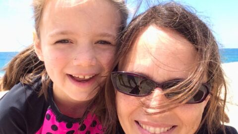 mom and girl looking at the camera with beach in background.