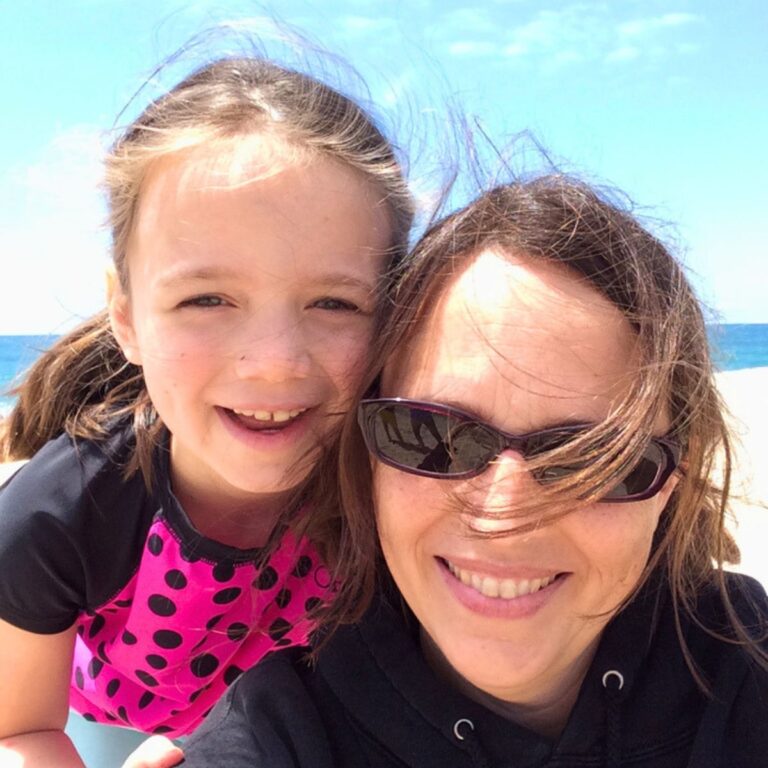 mom and girl looking at the camera with beach in background.