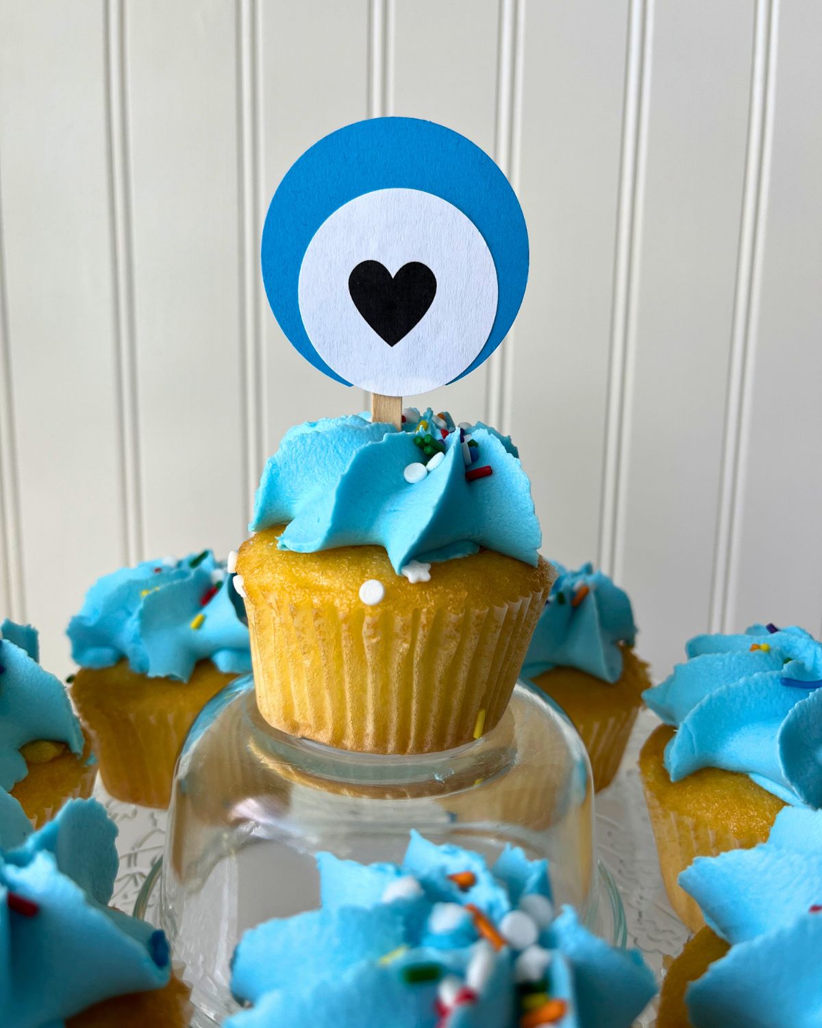 blue frosted cupcake with a heart cake topper inserted in the top.