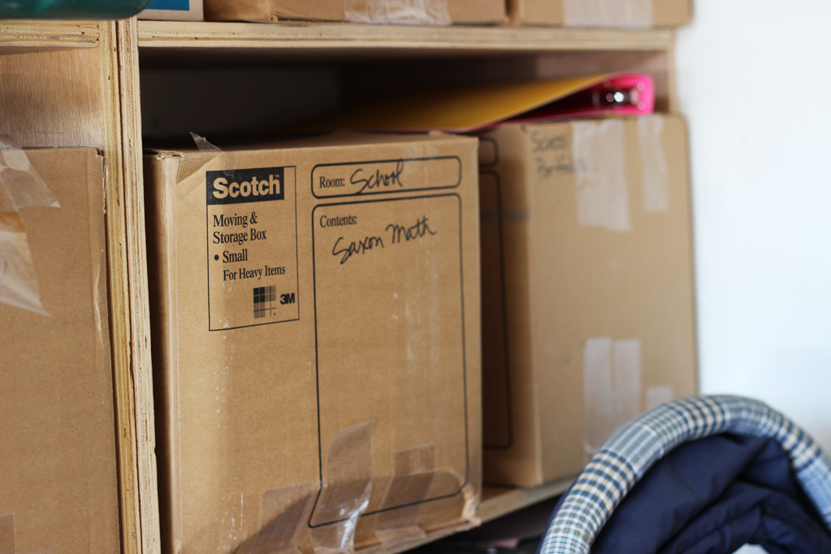 cardboard box labeled Saxon math on shelf in garage.