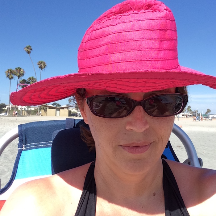 A woman wearing a hat and sunglasses posing for the camera at the beach.