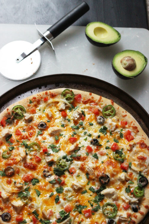 A pizza sitting on top of a pan on a table, with avocado halves
