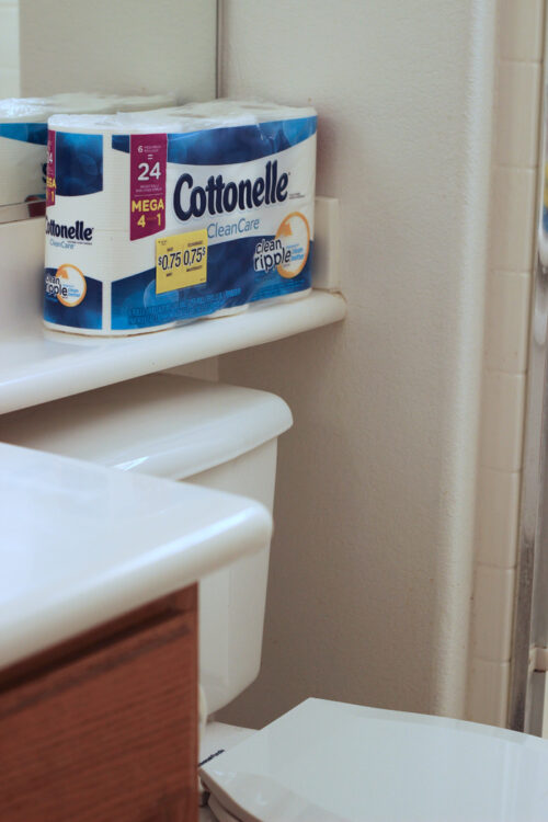 View of package of toilet paper on shelf above toilet.