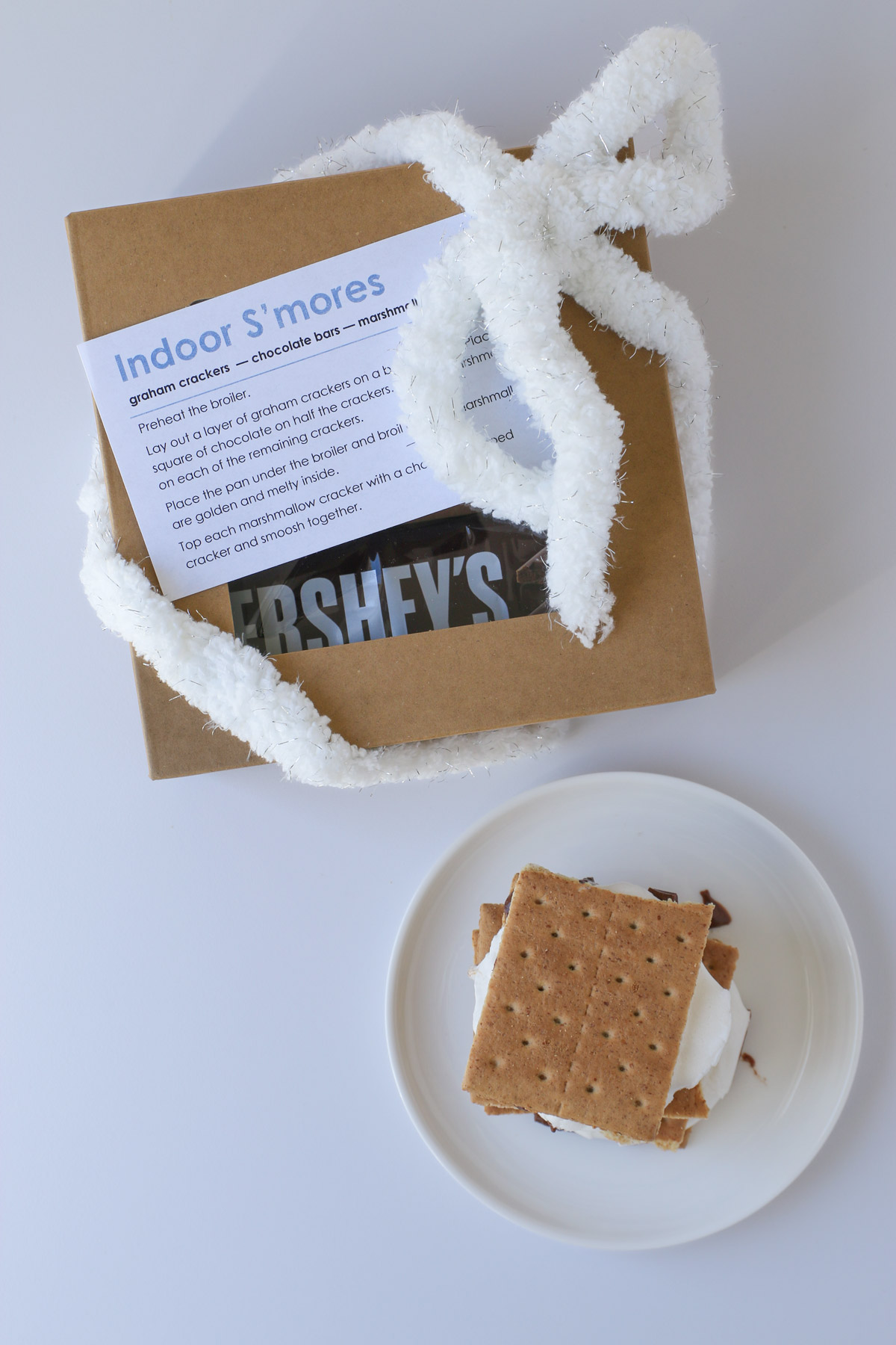 s'mores kit with recipe card attached and a cooked s'more on a plate nearby.
