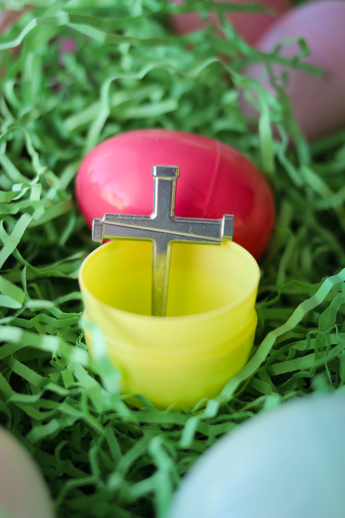 metal cross inside an open yellow plastic easter egg on a bed of grass with other plastic eggs.