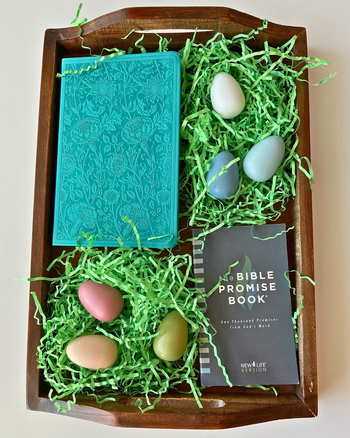 a wooden tray full of green paper grass, a teal bible, and a bible promise book.