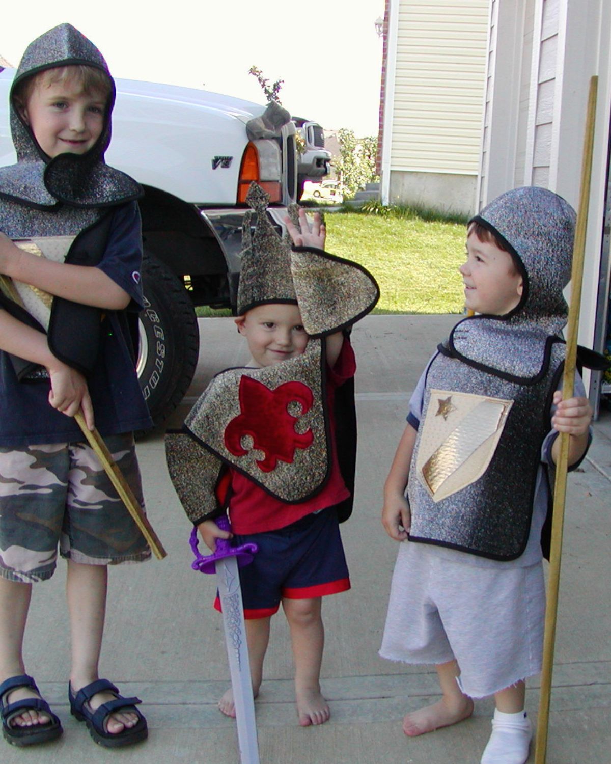 three boys dressed as knights playing in the driveway.