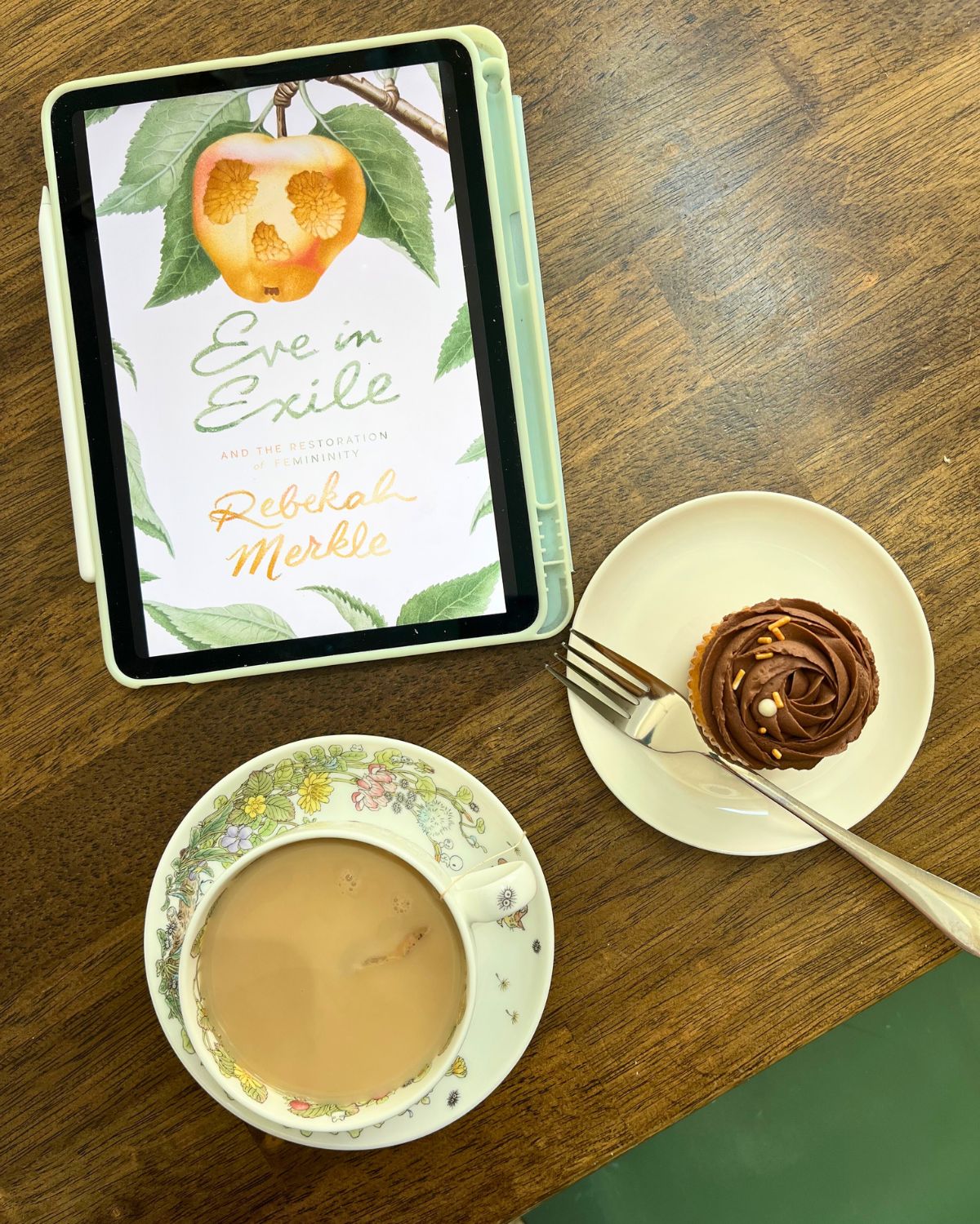 eve in exile on iPad next to cupcake and cup of tea.