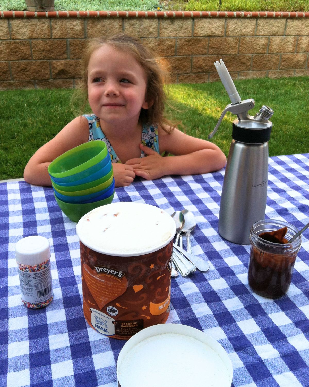 little girl waiting for ice cream sundaes at picnic table in backyard.