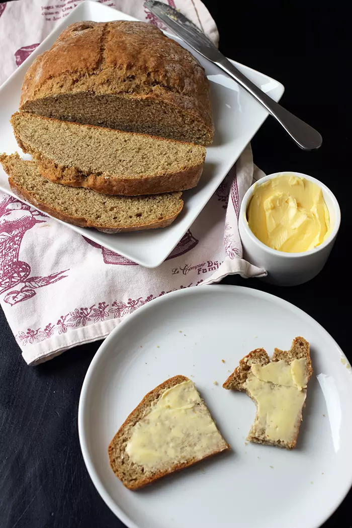 irish soda bread sliced on a tray with a dish of butter, a plate with a buttered slice is nearby.