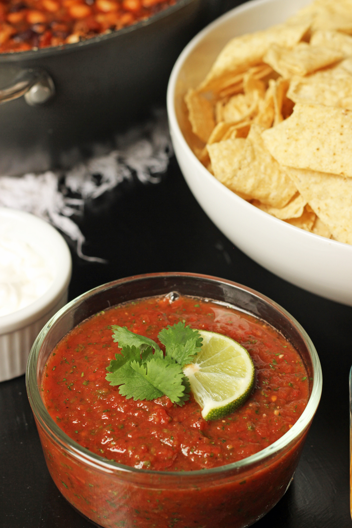 A bowl of salsa on a table, with chips and sour cream