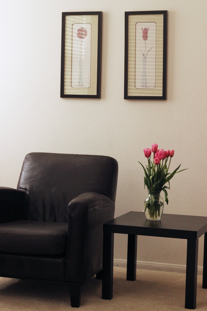 tulip paintings on wall behind arm chair and table with vase of tulips