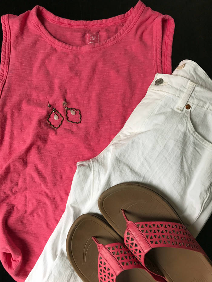 coral blouse with white jeans, earrings, and pink sandals on table.