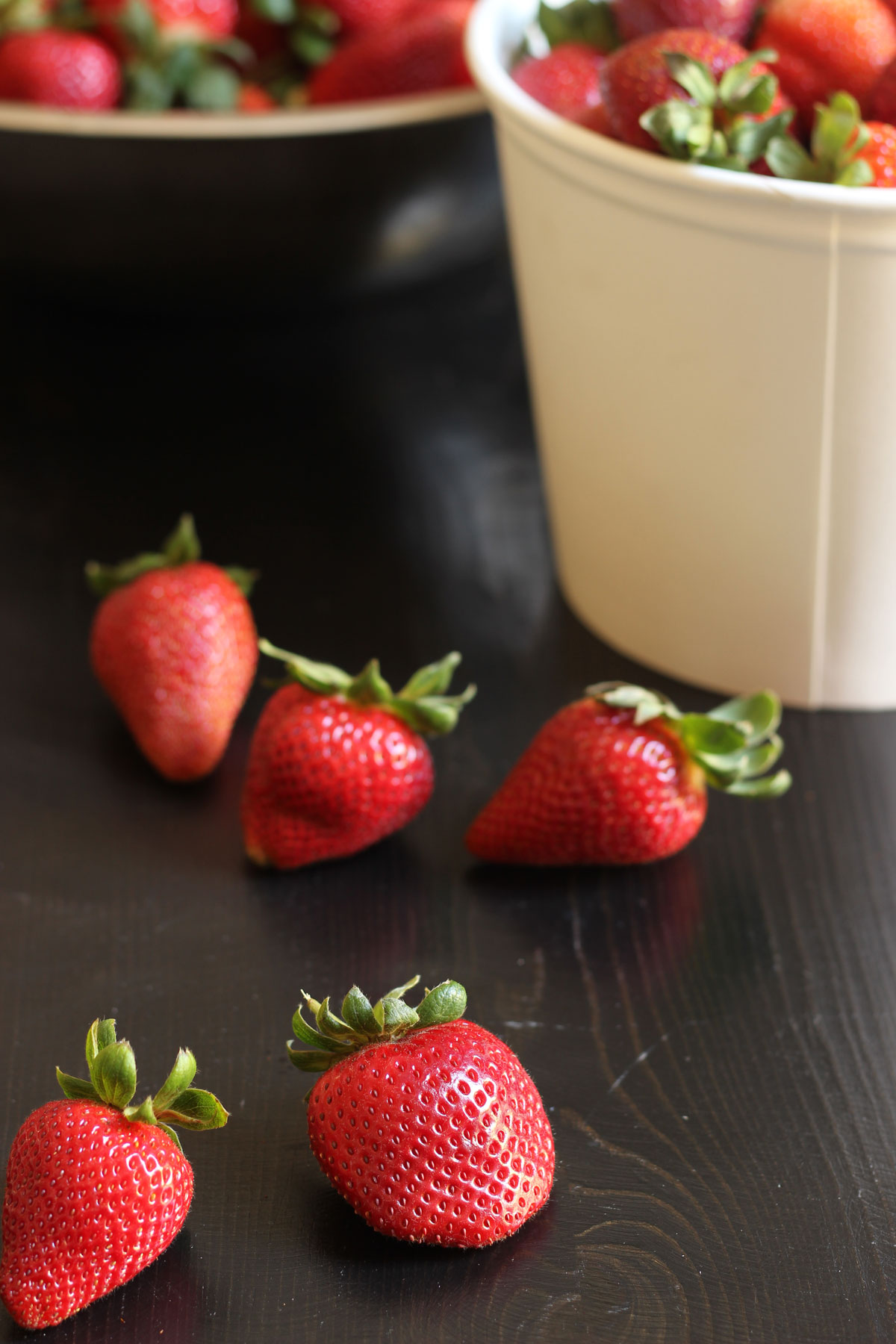 bucket of strawberries next to scattering of berries on black table top.