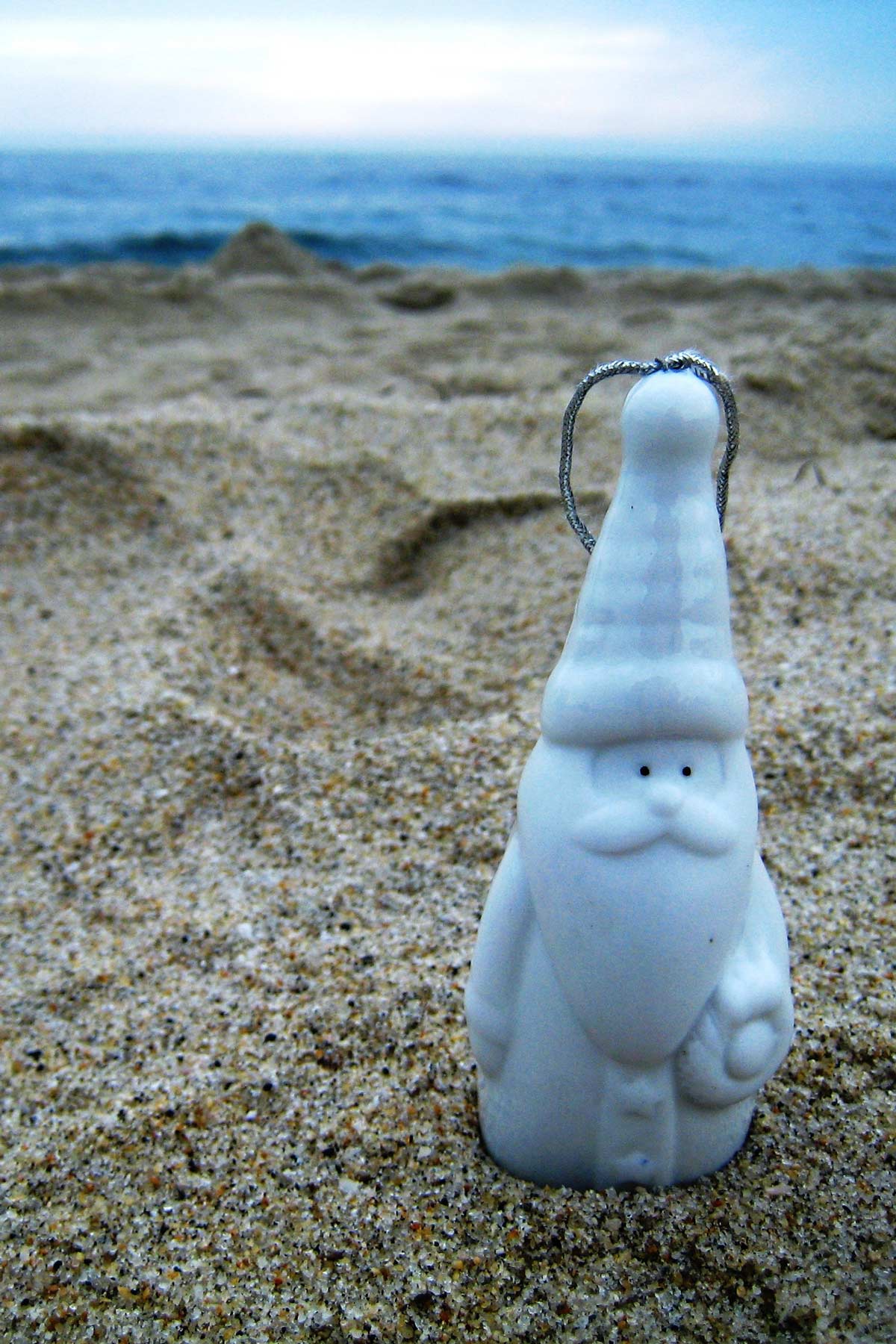 white santa claus ornament in sand at the beach.