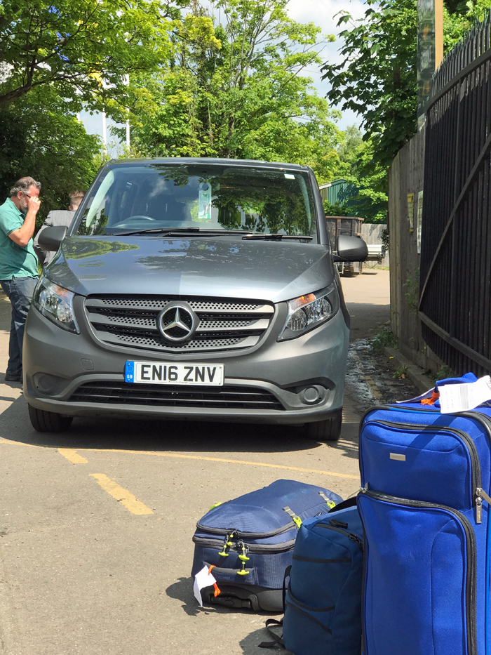 Luggage sitting in front of rental van in parking lot.