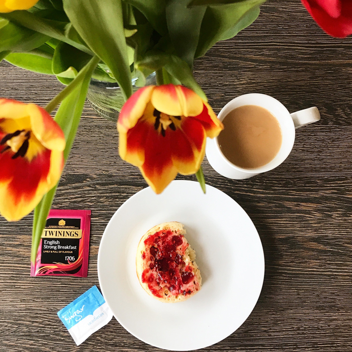 A plate of crumpet and jam, with tea and flowers