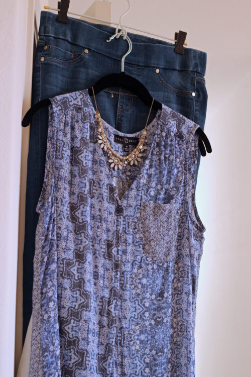 blue blouse and jeans on hangers with a necklace over top.