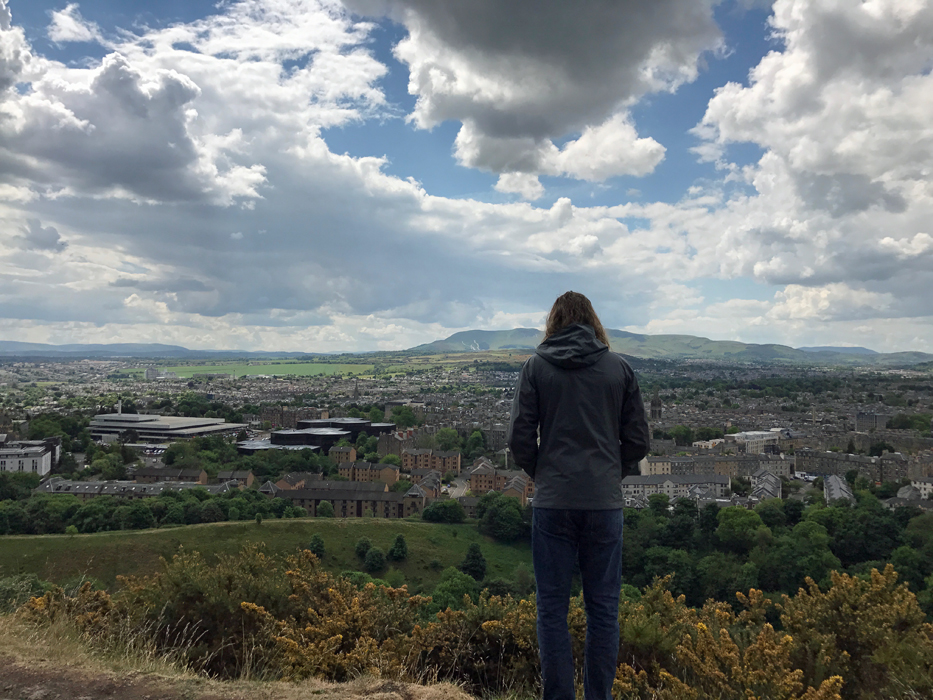 A man standing on top of Arthur\'s Seat in Edinburgh looking into the distance.