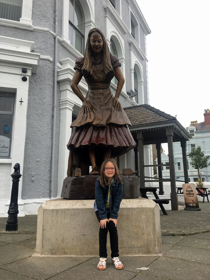 A girl kneeling next to statue of a Alicein Wonderland.