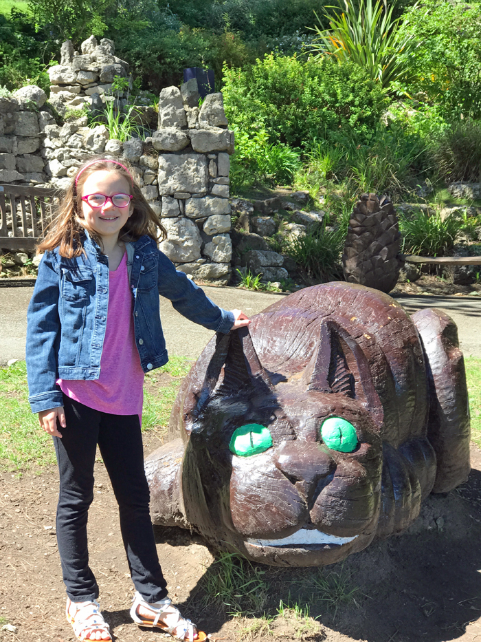 A girl standing next to a statue of the Cheshire Cat.