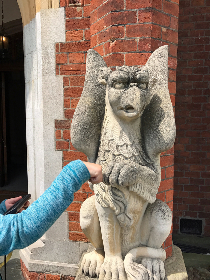 A statue of a gargoyle in front of a brick building with child fist bumping.