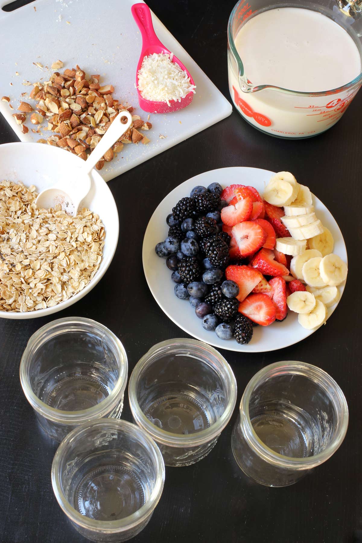empty jars on table with bowl of oats, prepped fruit, and coconut milk.