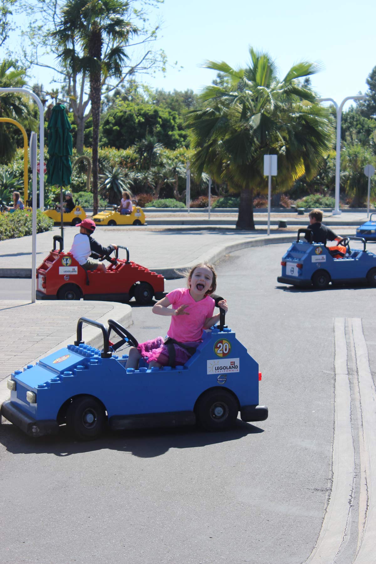 girl in pink shirt excited to drive a car at legoland.