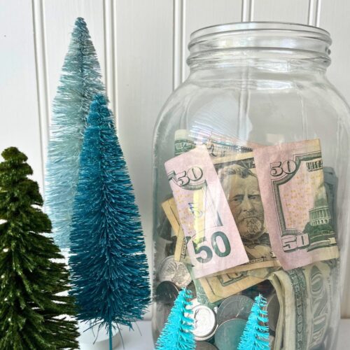 large jar of money near bottle brush Christmas tree decor.