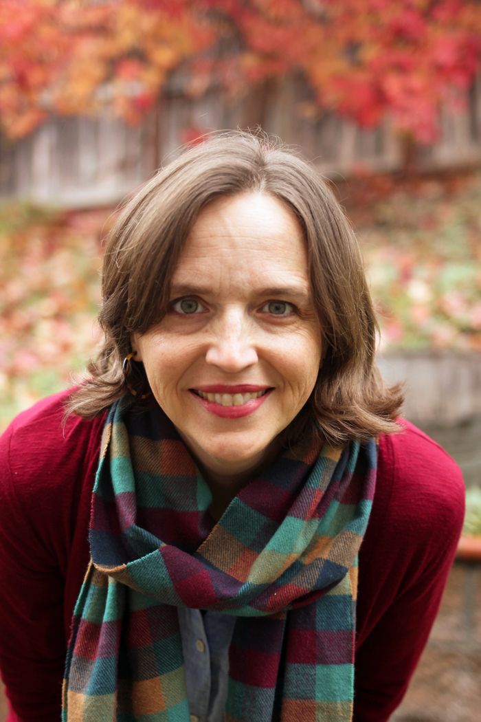 brunette woman with plaid scarf in front of fall trees