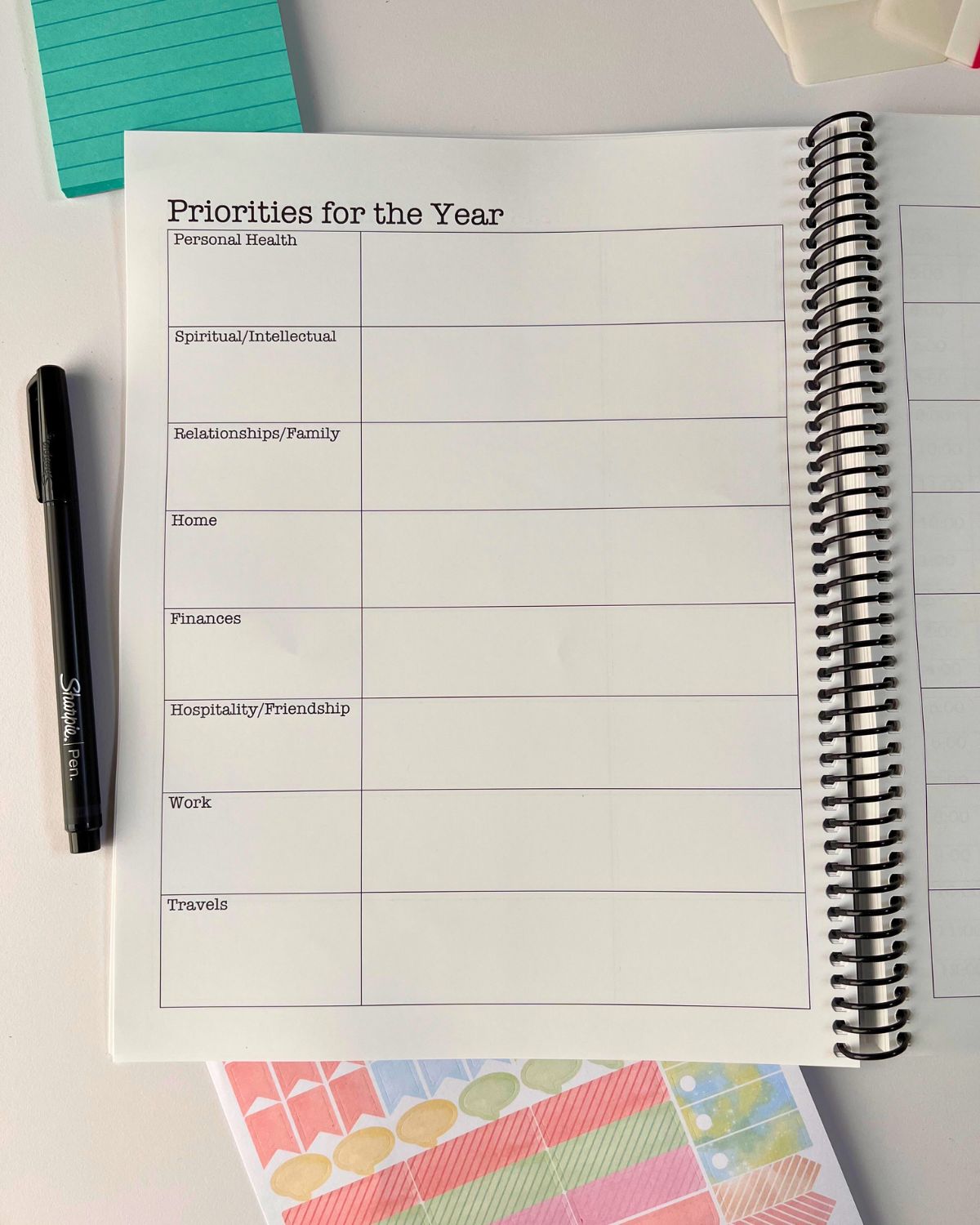 spiral-bound planner open to priorities for the year page on table with pen and stickers nearby.