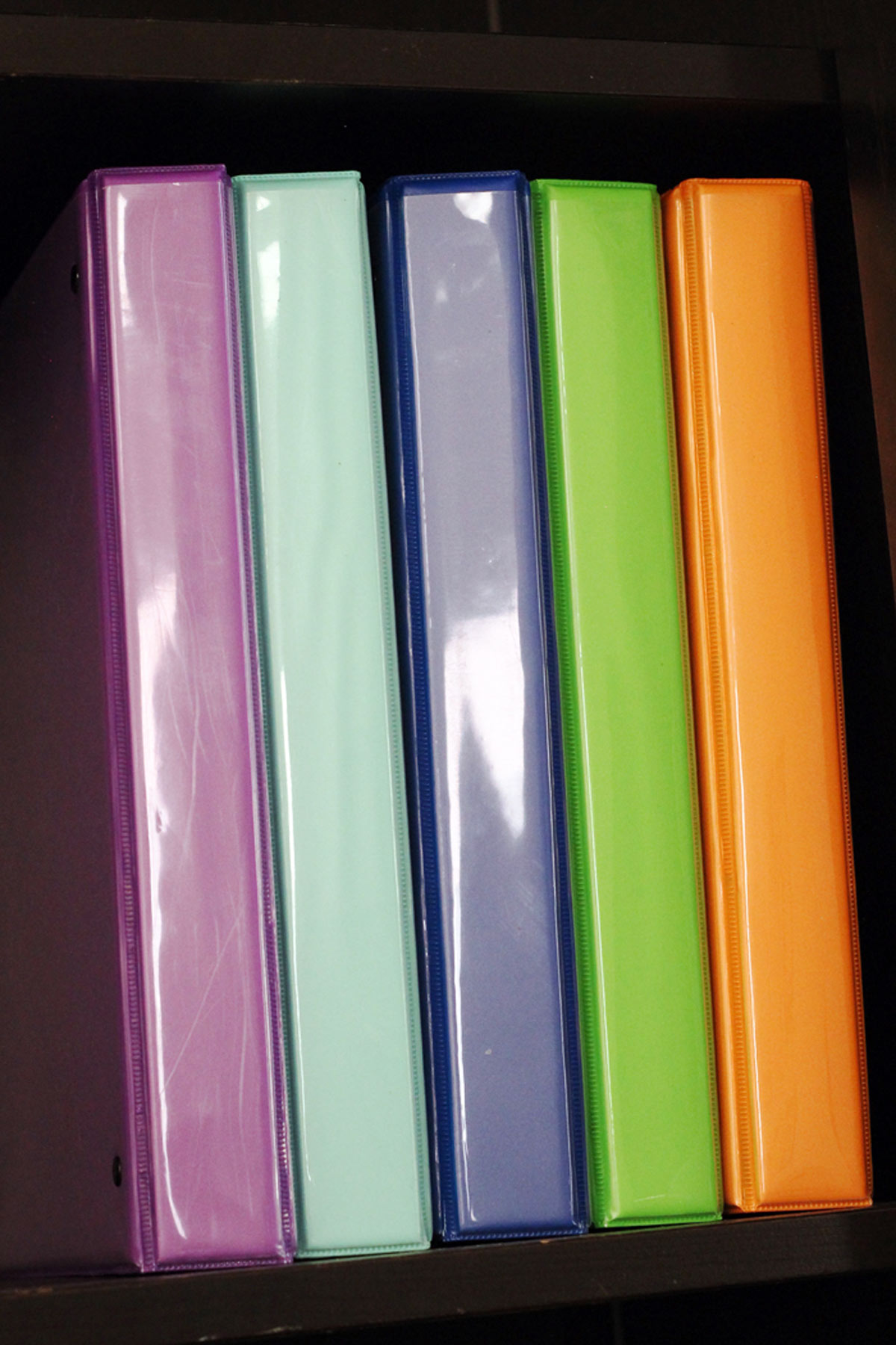 colored binders on a black bookshelf.