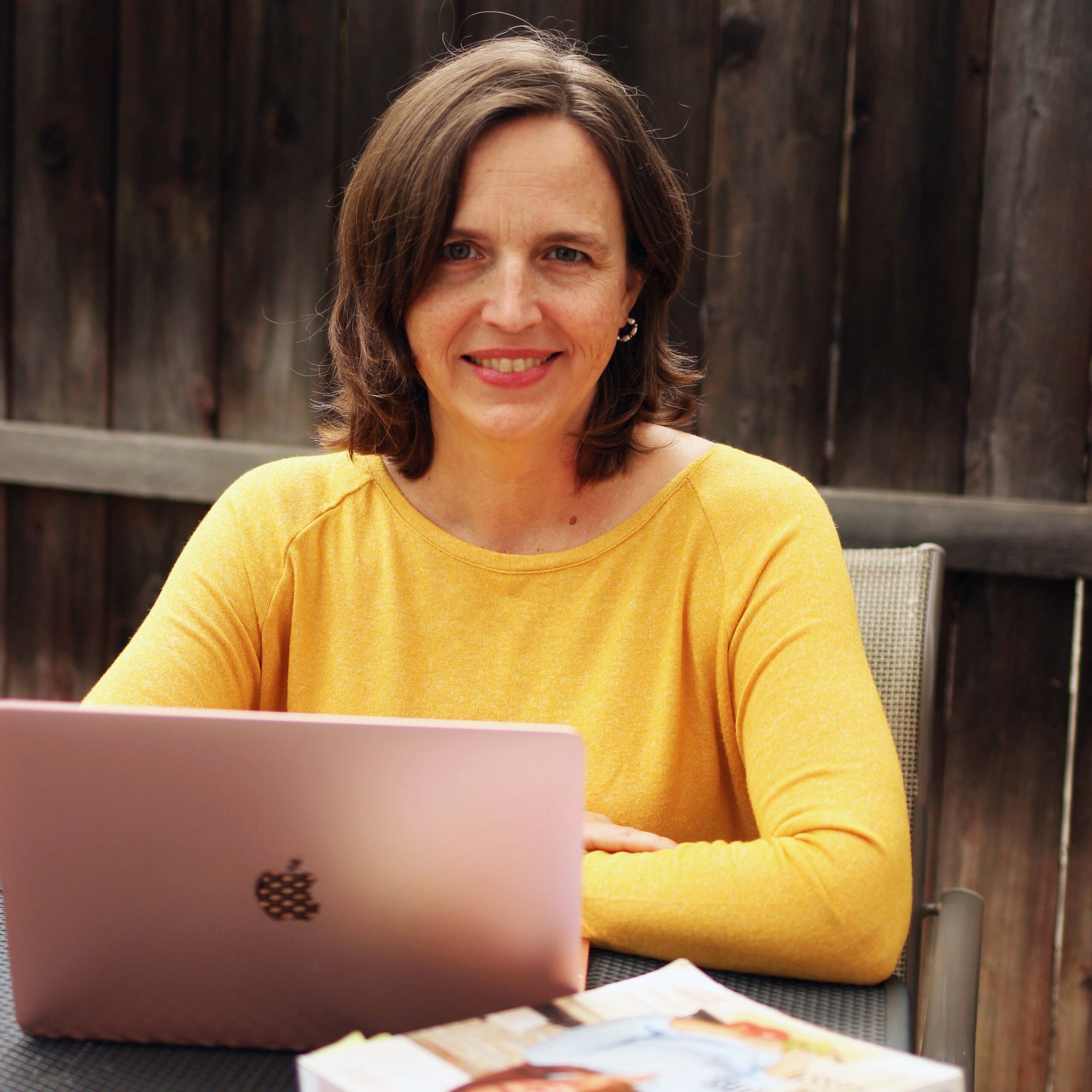 A woman sitting at a table with a laptop and smiling at the camera