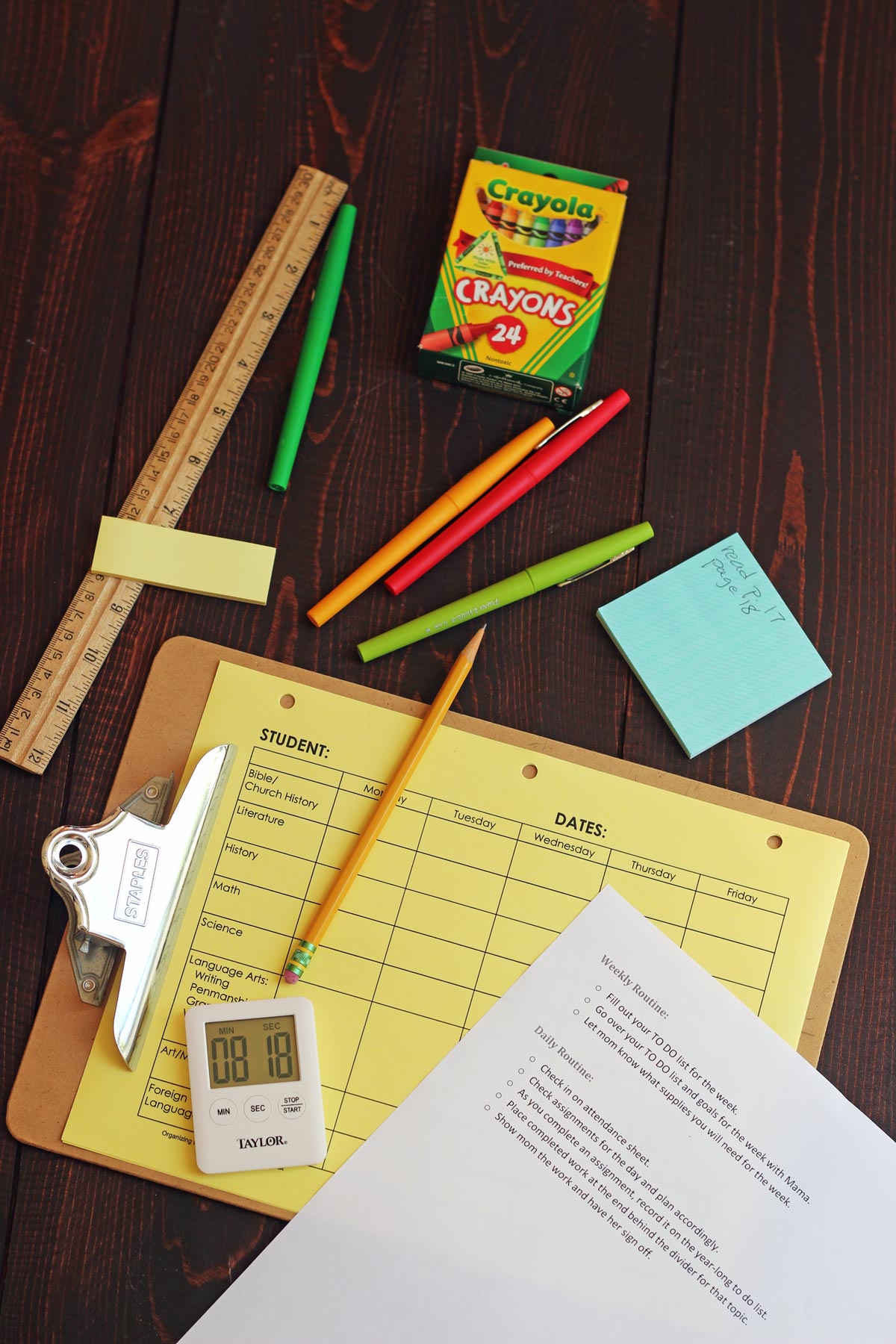 school supplies including clipboard on red wood table.